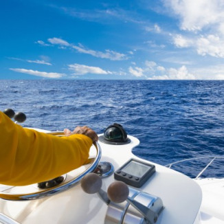 Hand on steering wheel of motor boat on the ocean
