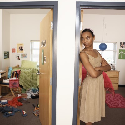 Young woman standing in doorway of neat dorm room, looking to side 