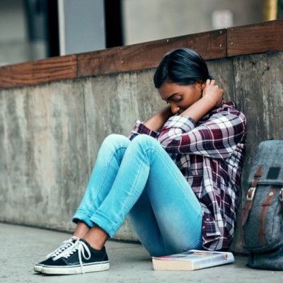 Young woman sitting on the sidewalk with her head in her hands.