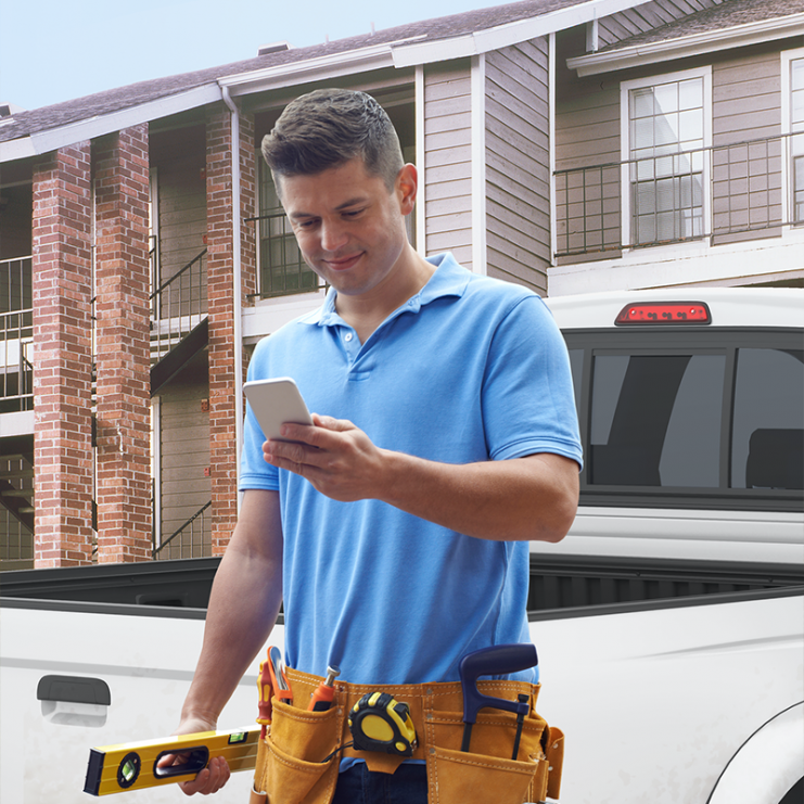 Man in blue polo standing in front of apartment building looking at phone